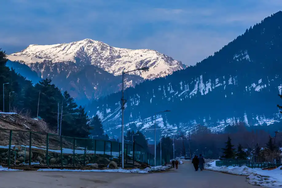 Romantic couple enjoying a winter honeymoon in Pahalgam, surrounded by snow-clad mountains and Lidder River, part of Kashmir Nirvana’s Luxury Kashmir Honeymoon Package.
